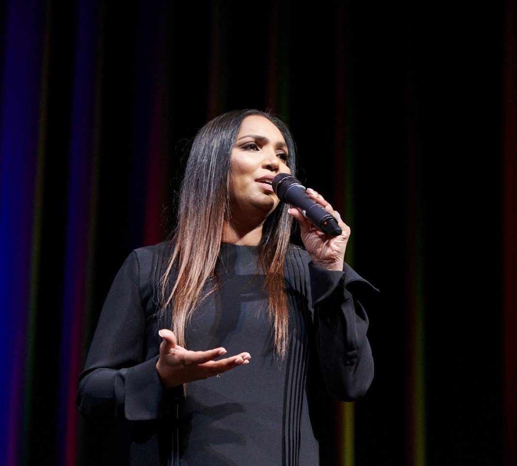 Norliza on stage — international keynote speaker with rainbow stage lighting, microphone in hand